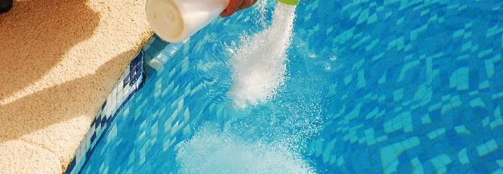 Person gibt Poolchemikalien in den Pool